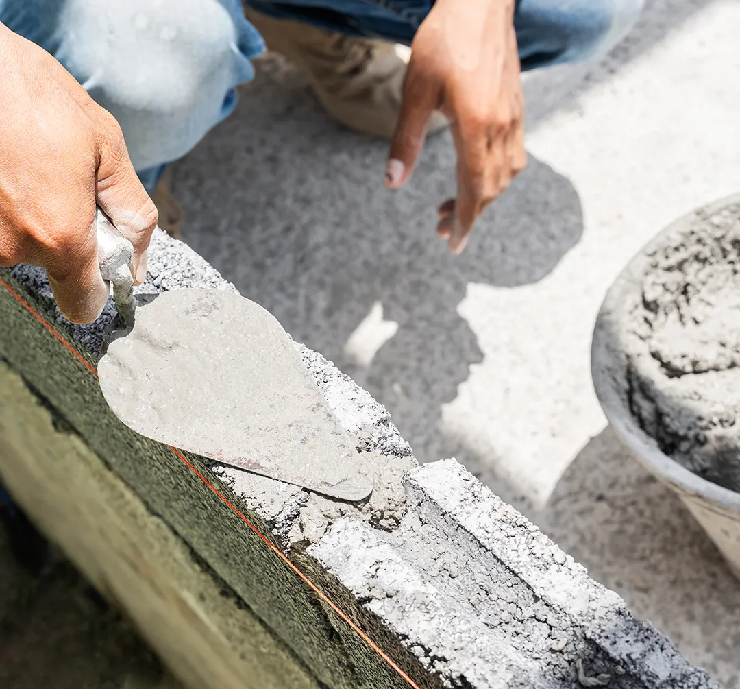 Construction worker applying fresh cement mortar to a masonry surface with a trowel