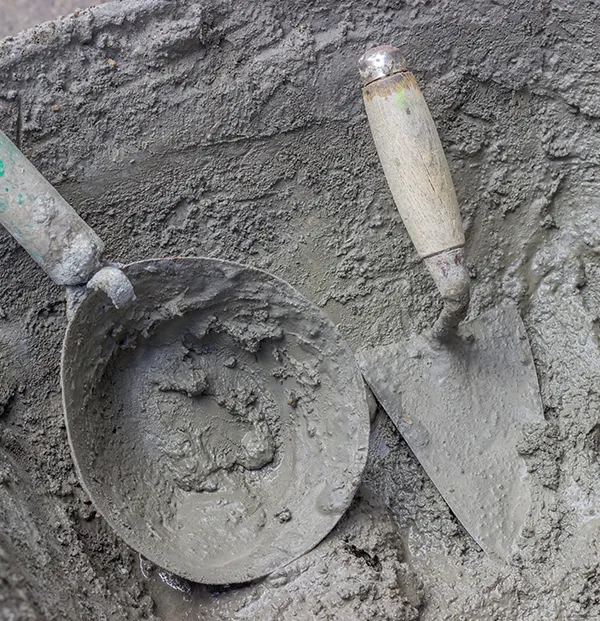 Fresh cement mortar in a mixing bucket surrounded by hand trowels
