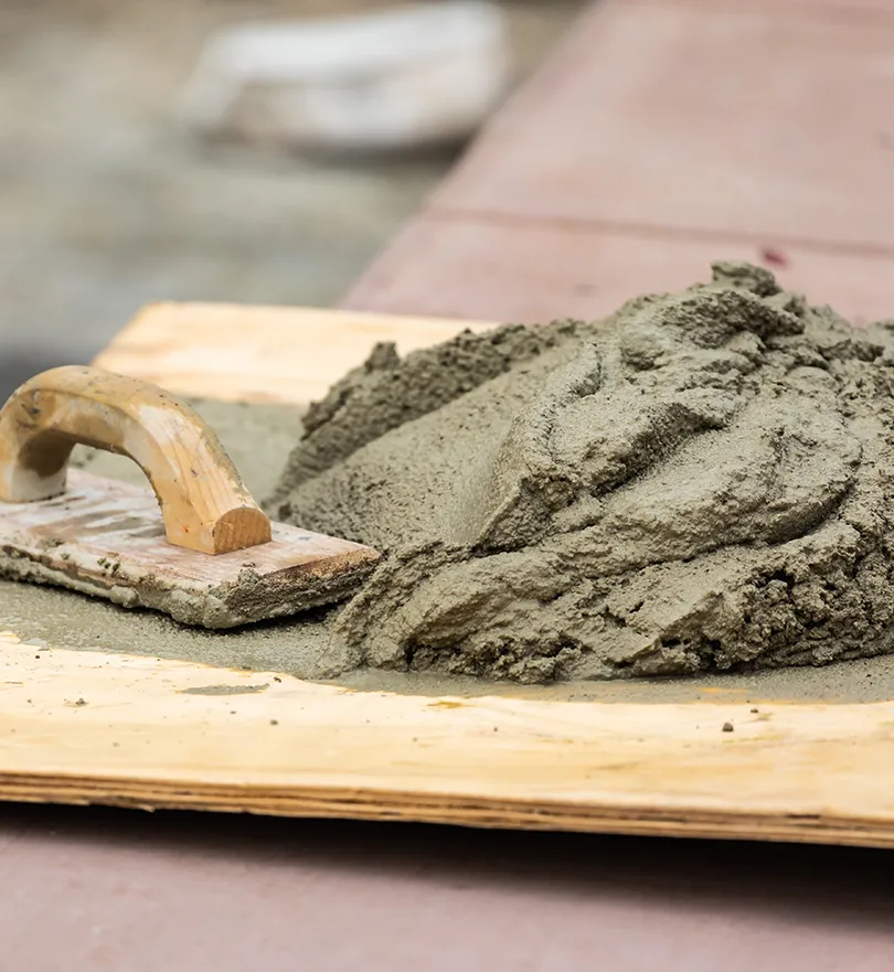 Fresh cement mortar placed on a wooden mixing board beside a hand trowel